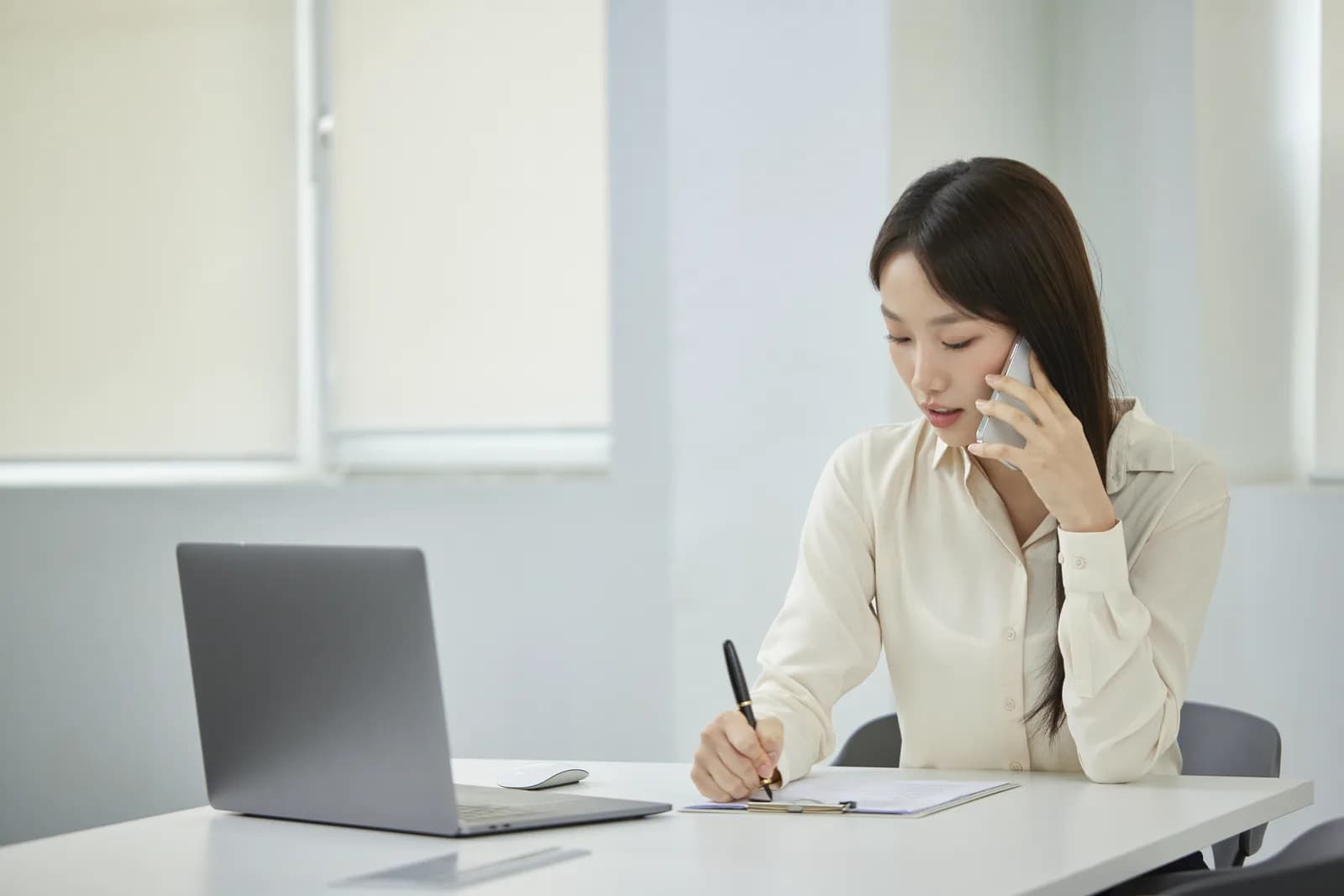 책상에서 전화로 상담하며 메모하는 여성